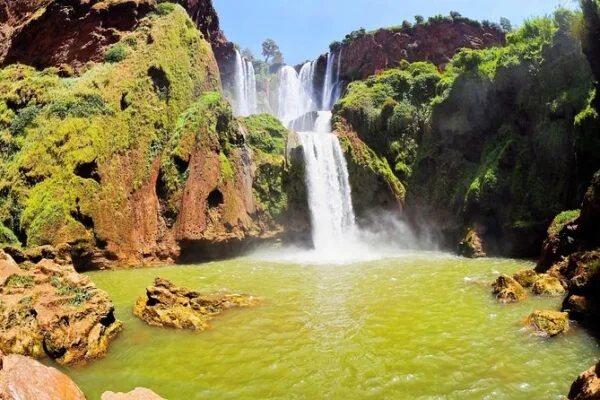 A stunning view of a large waterfall cascading into a vibrant green pool, surrounded by rocky cliffs covered in lush vegetation.